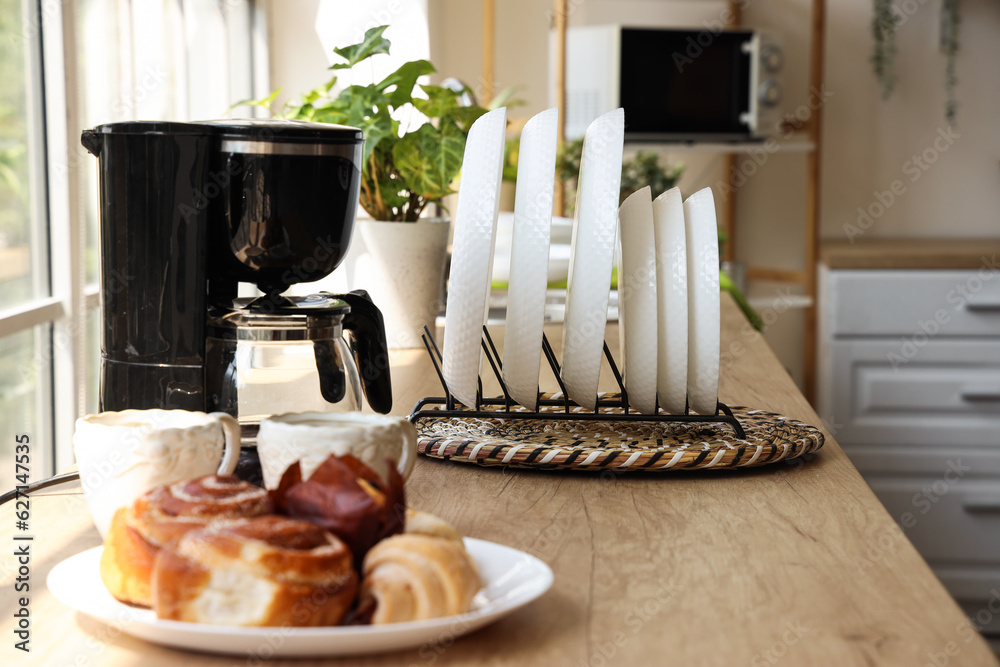 Plate rack, coffee machine, cups and pastry on wooden counter