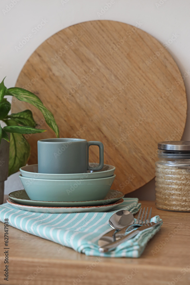 Clean dishes, houseplant, cutlery and jar on wooden counter