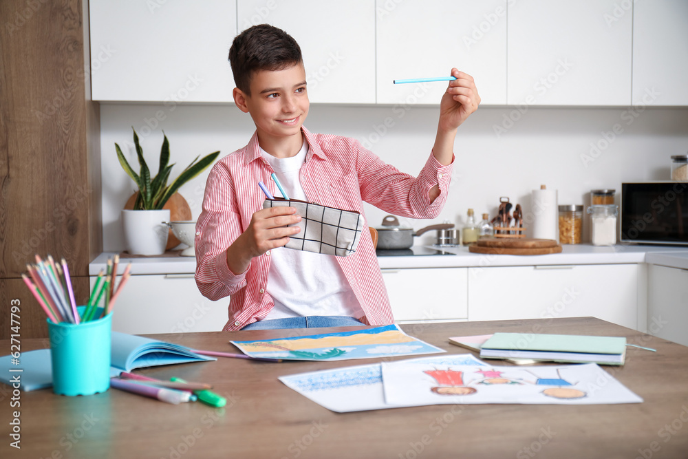 Little boy with pencil case at table in kitchen