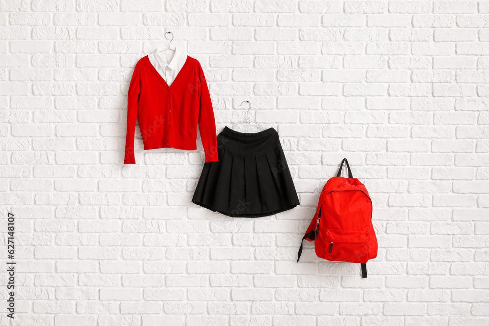 Stylish school uniform and backpack hanging on light brick wall in room