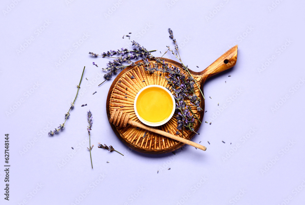 Wooden board with bowl of sweet lavender honey, dipper and flowers on blue background