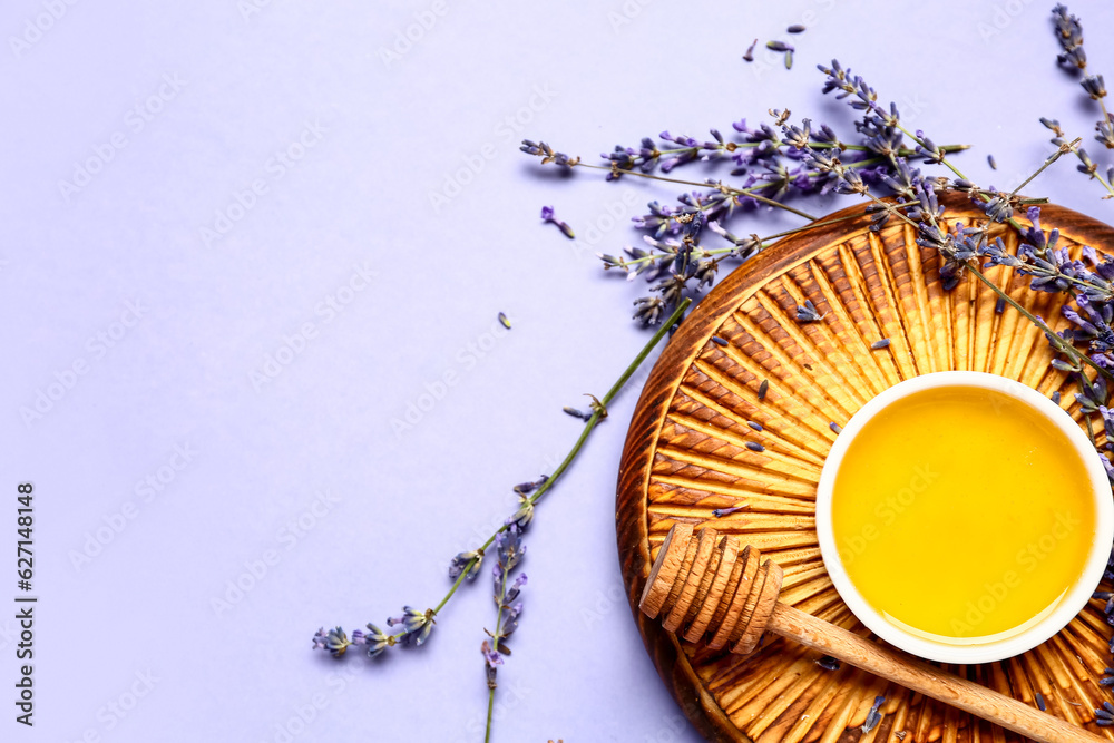 Wooden board with bowl of sweet lavender honey, dipper and flowers on blue background