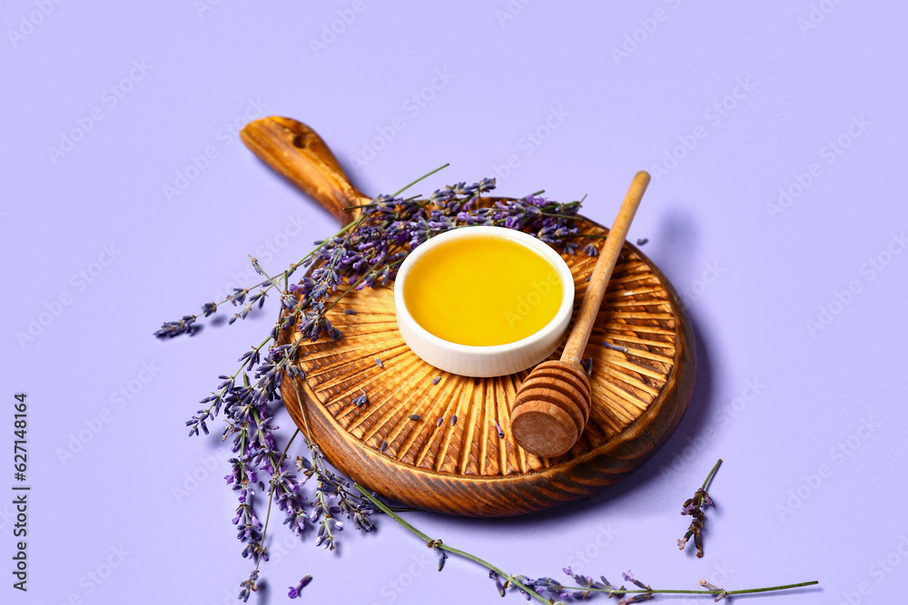 Wooden board with bowl of sweet lavender honey, dipper and flowers on blue background