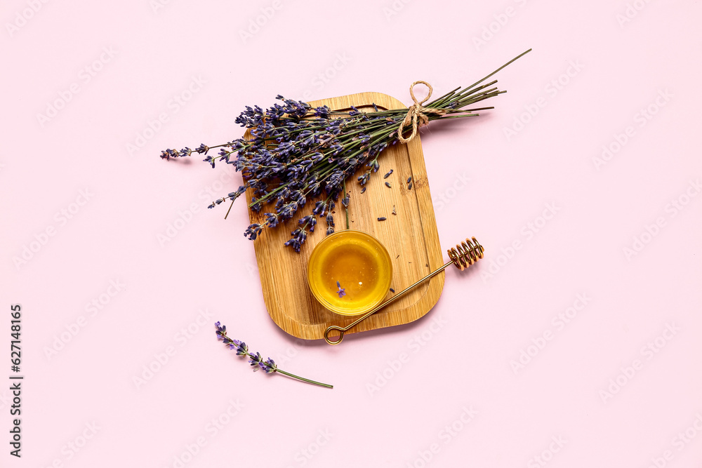 Wooden board with glass bowl of sweet lavender honey, dipper and flowers on pink background