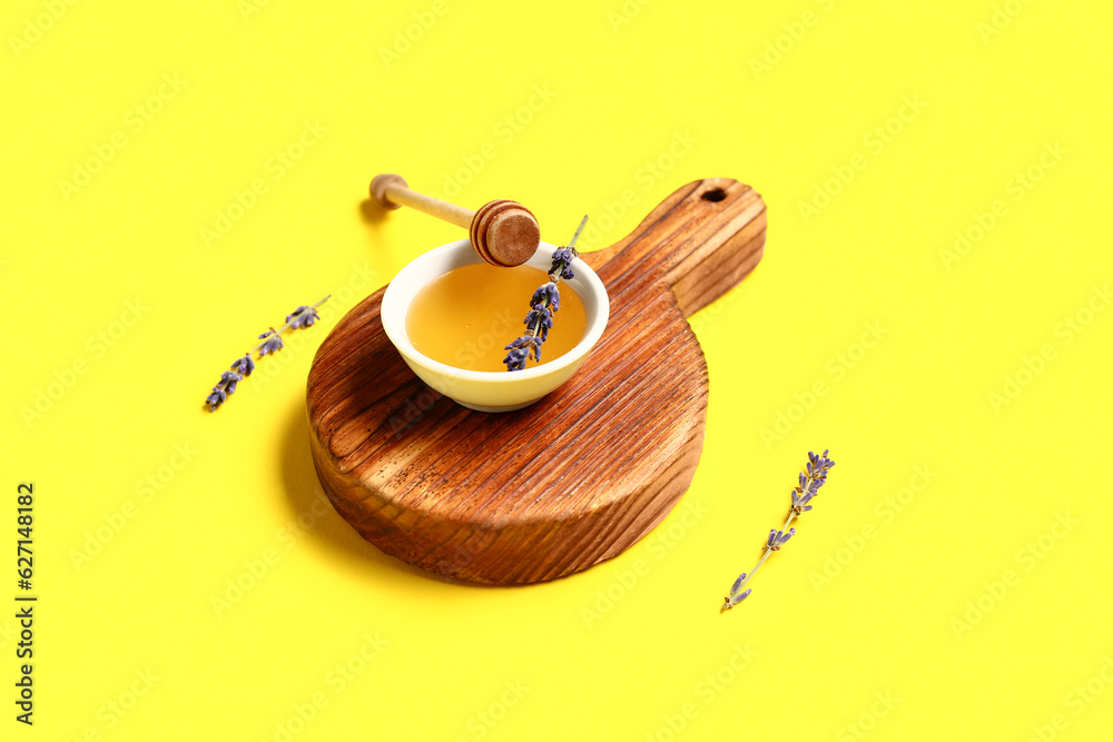 Wooden board with bowl of sweet lavender honey, dipper and flowers on yellow background