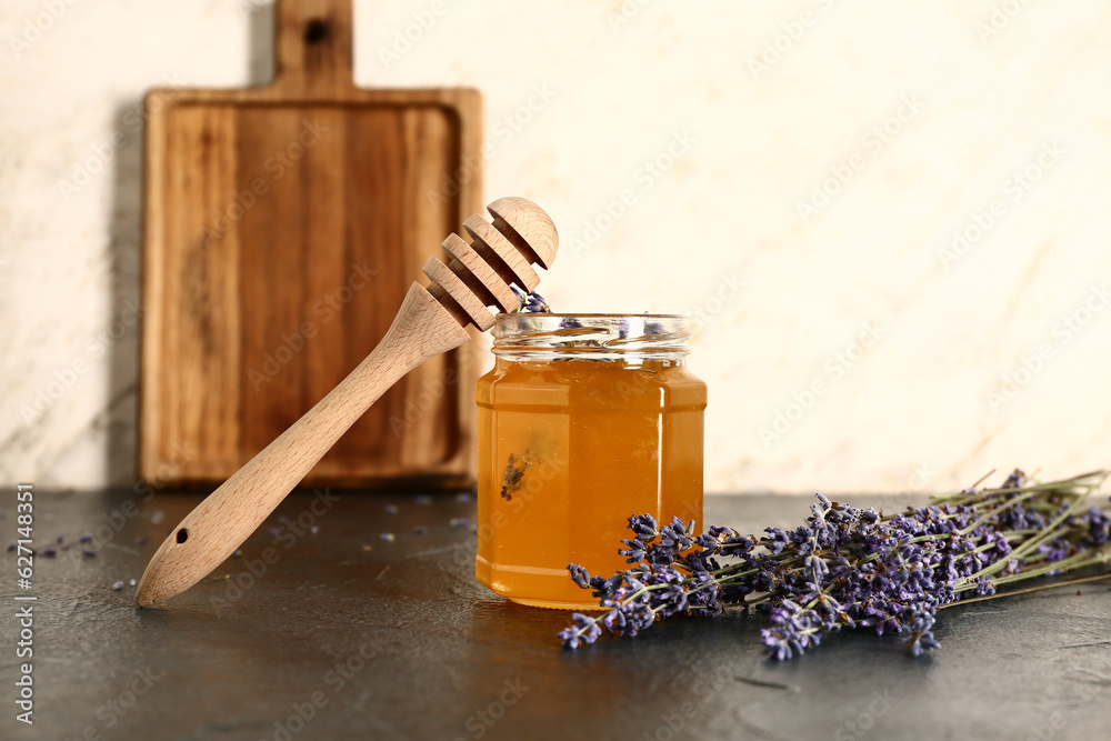 Jar of sweet lavender honey, dipper and flowers on dark table