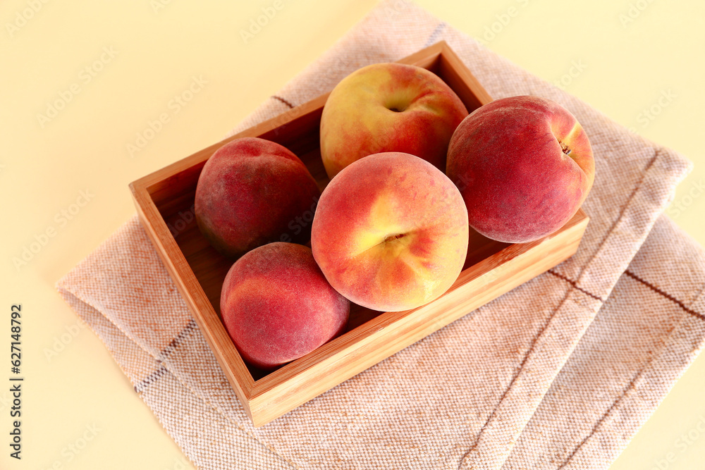 Wooden box with sweet peaches on yellow background