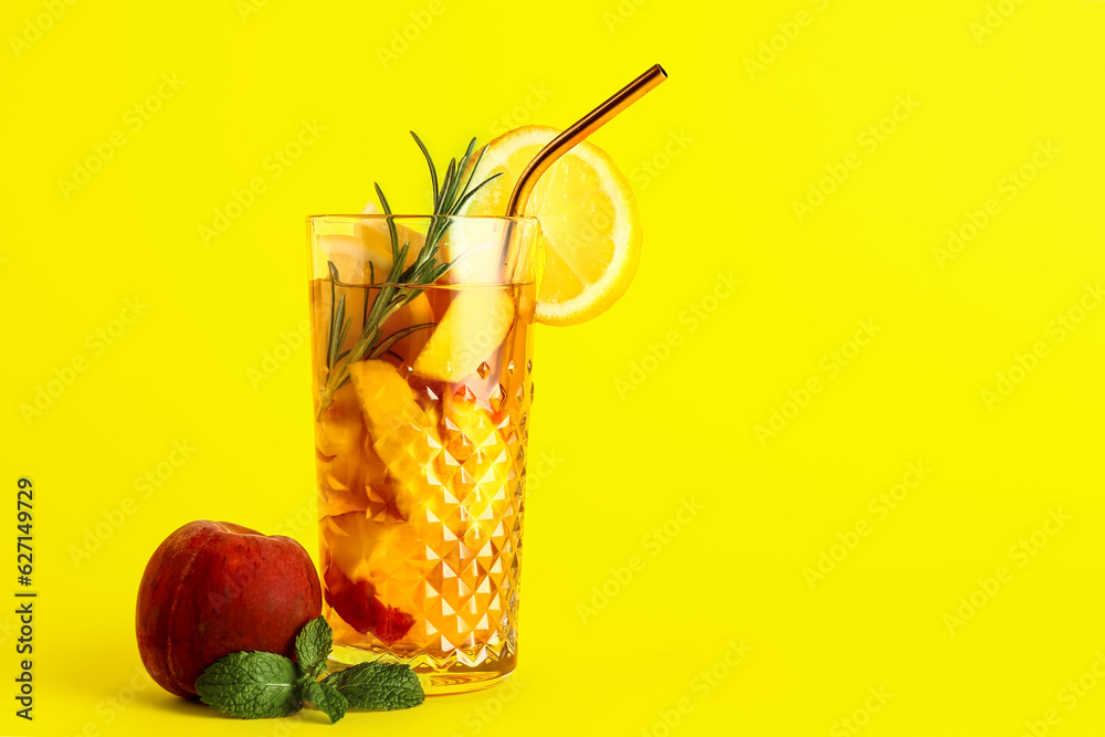 Glass of fresh peach lemonade with rosemary and mint on yellow background