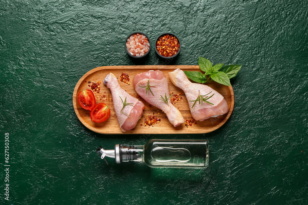 Wooden board with raw chicken legs, spices and oil on color background