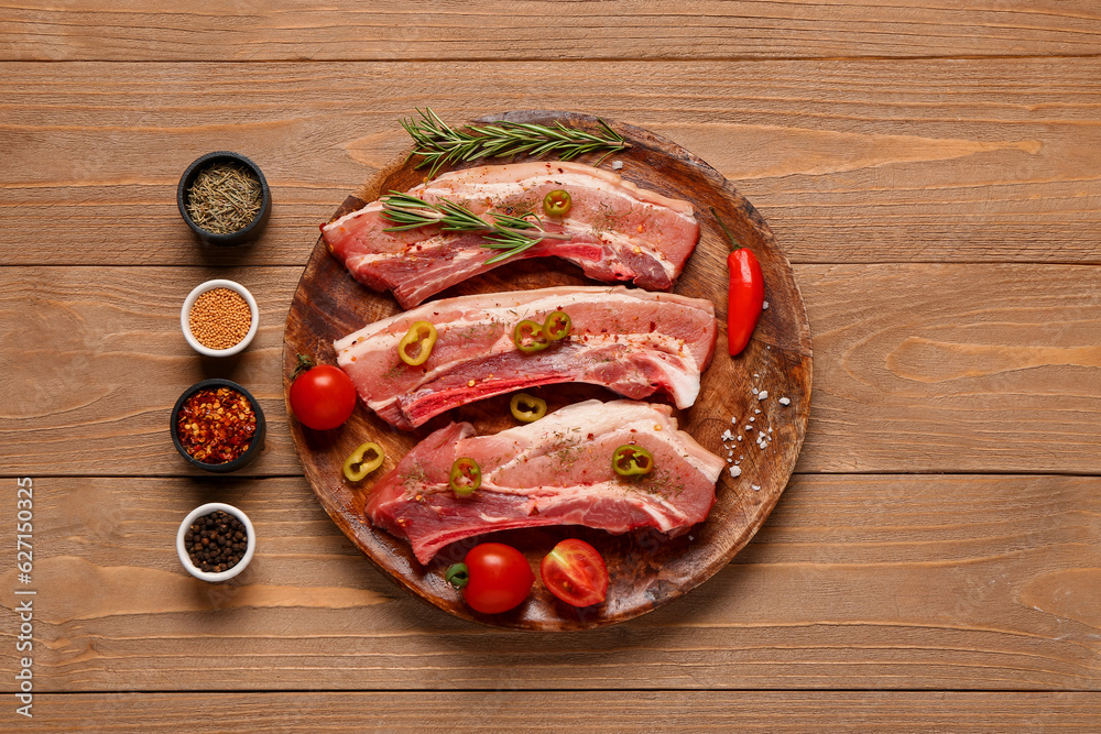 Plate with raw pork ribs, tomatoes and different spices on wooden background