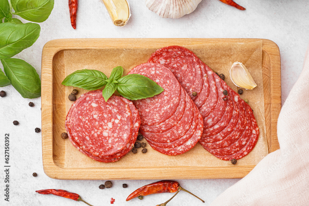 Wooden board with slices of tasty salami on light background