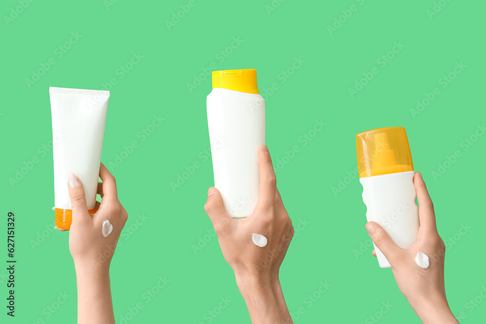 Female hands with bottles of sunscreen cream on green background