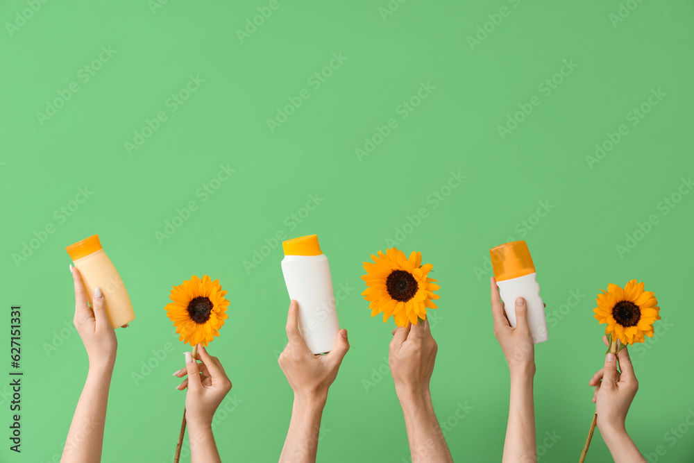 Female hands with bottles of sunscreen cream and sunflowers on green background