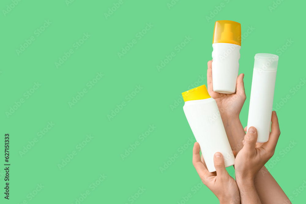 Female hands with bottles of sunscreen cream on green background