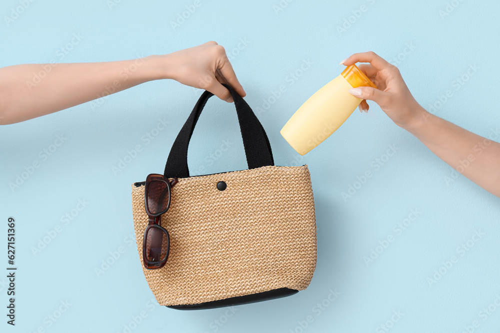 Female hands with bottle of sunscreen cream and bag on blue background