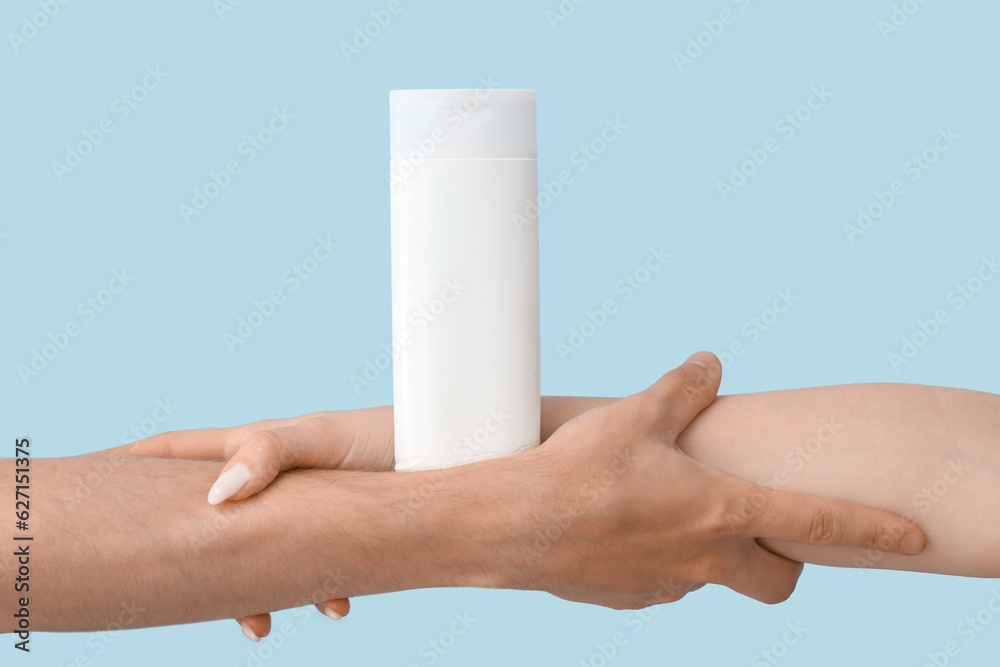 Female hands with bottle of sunscreen cream on blue background