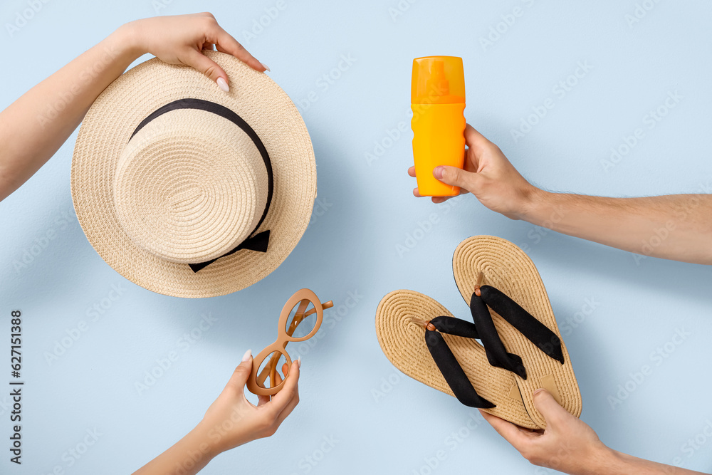 Female hands with sunscreen cream, hat, sunglasses and flip flops on blue background