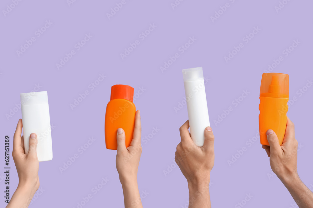 Female hands with bottles of sunscreen cream on lilac background