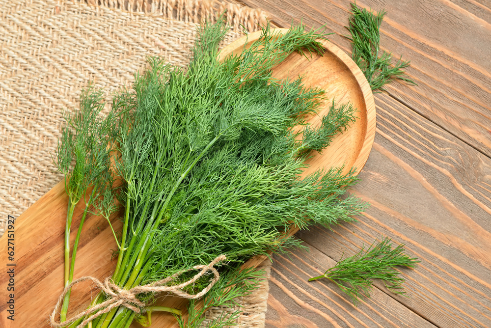 Board with bunch of fresh dill on wooden background