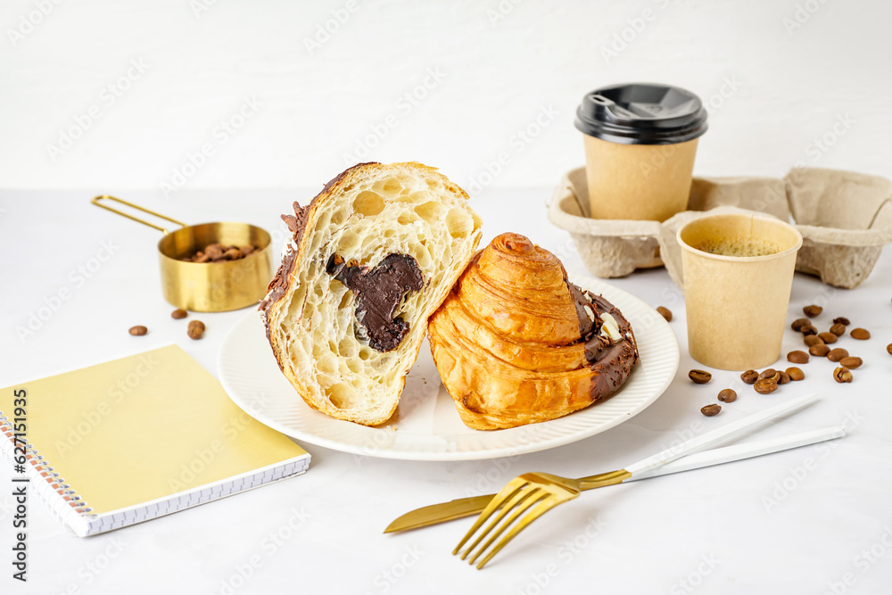 Plate with tasty chocolate croissant and cups of coffee on light background