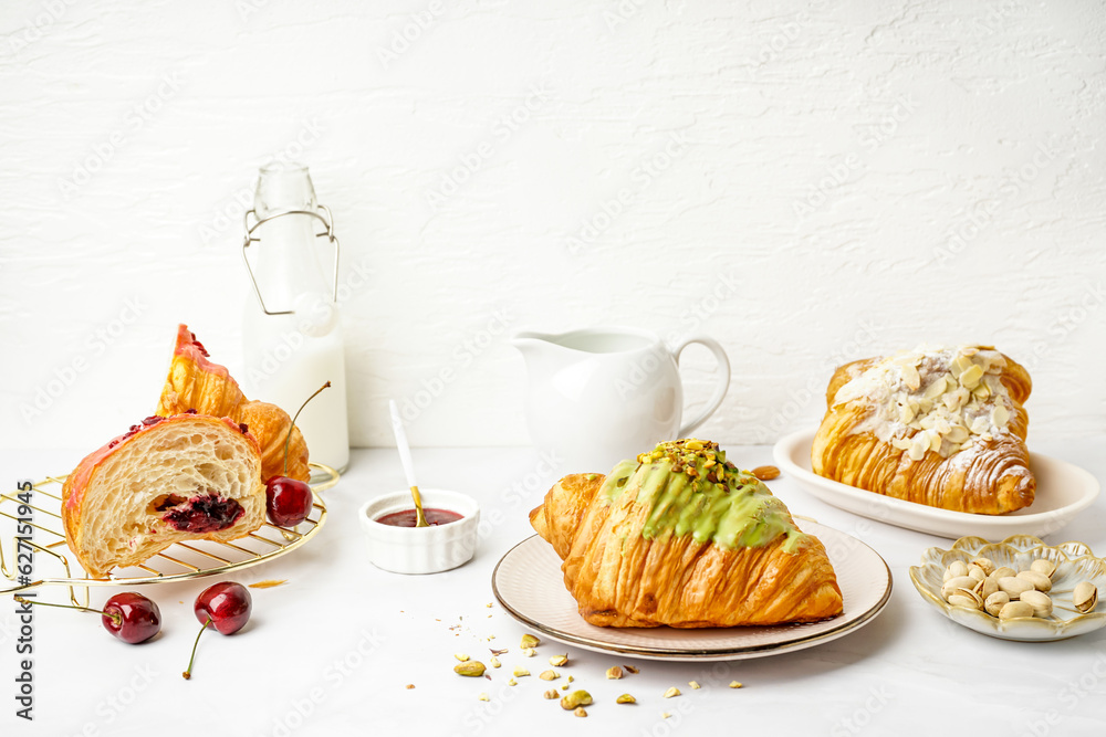 Tasty croissants, jam and pistachio nuts on light background