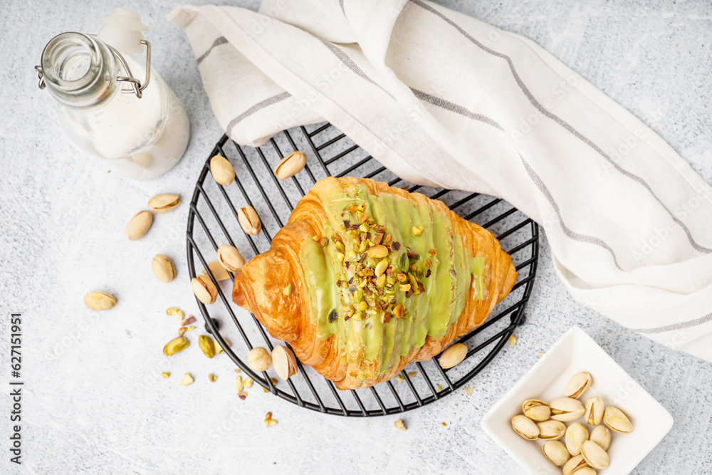 Grid with tasty croissant and pistachio nuts on white background