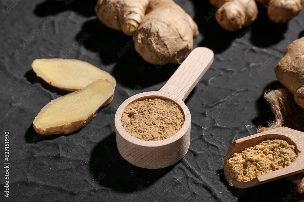 Fresh ginger roots, wooden spoon and scoop with dried powder on black background