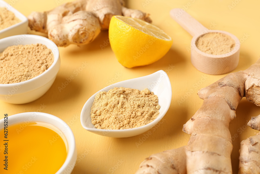 Fresh ginger roots, lemon and bowls with dried powder on yellow background