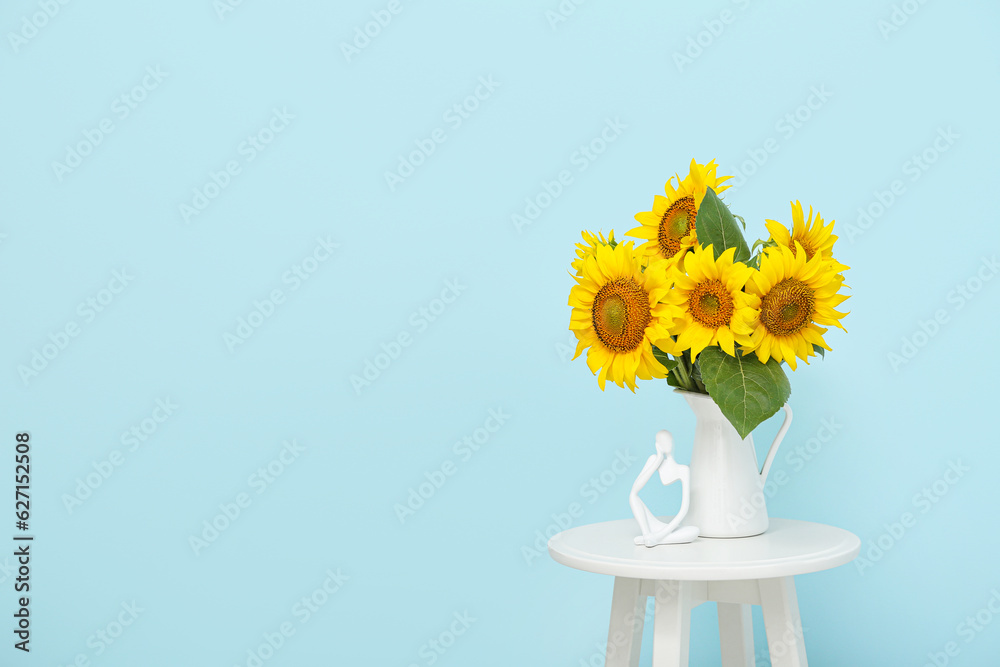 Vase with beautiful sunflowers on table near blue wall in room