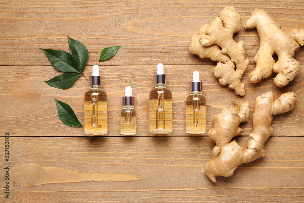 Bottles of ginger cosmetic oil and leaves on wooden background