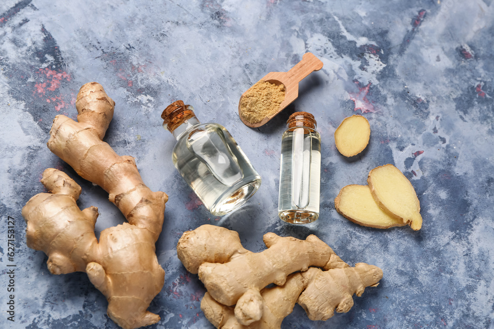 Bottles of ginger cosmetic oil and wooden scoop with dried powder on blue background