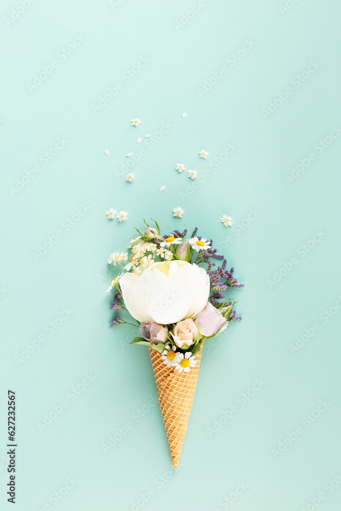 Flat-lay of waffle cone with flowers over pastel light blue background, top view