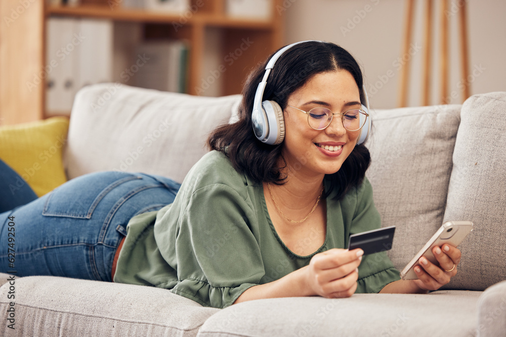 Woman, credit card and phone on sofa, home and headphones with smile, online shopping or payment on 