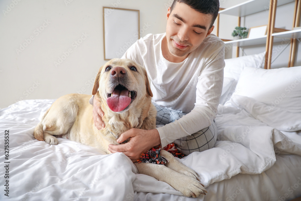 Young man with cute Labrador dog and toy sitting in bedroom