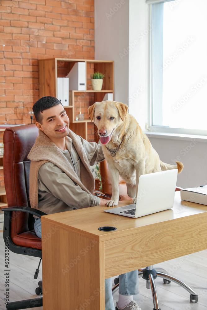 Young man with cute Labrador dog at table in office