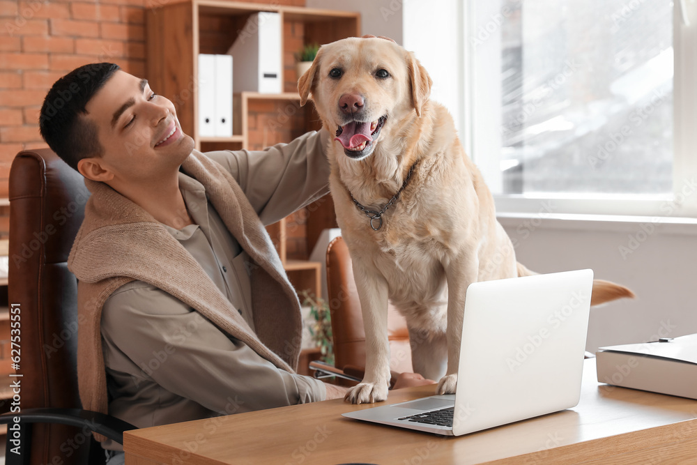 Young man with cute Labrador dog at table in office