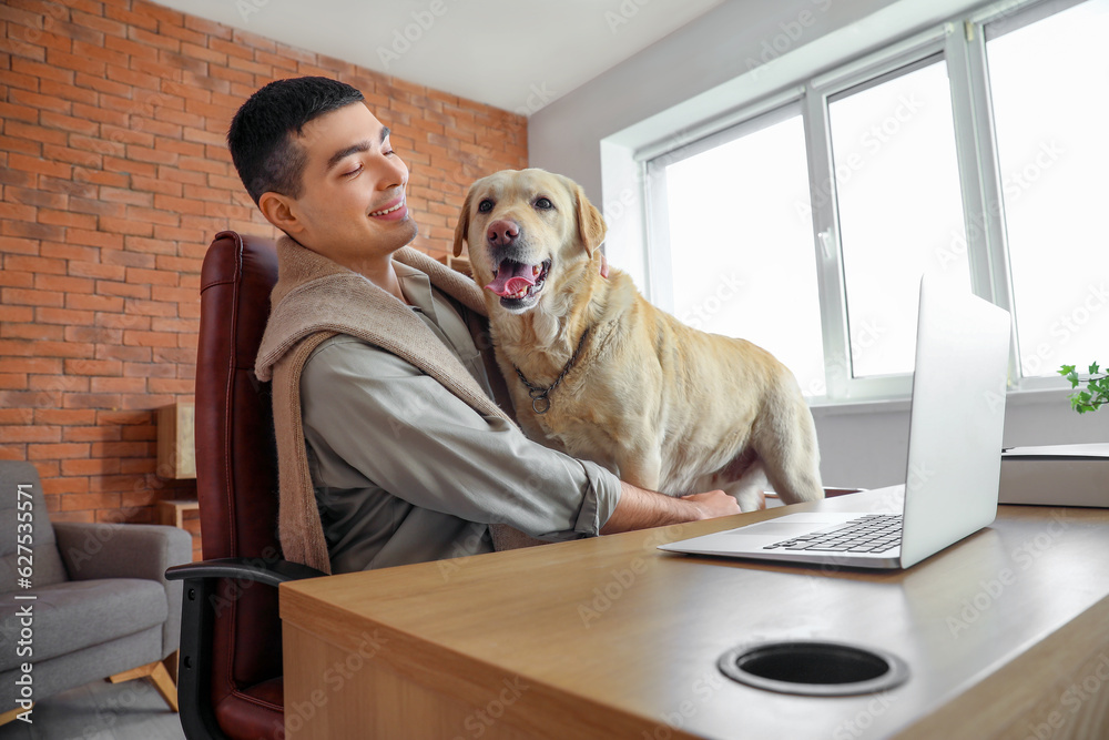 Young man with cute Labrador dog at table in office