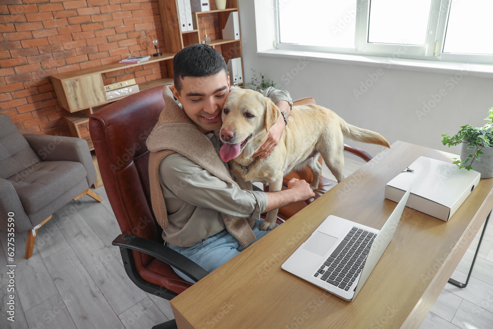 Young man hugging cute Labrador dog at table in office