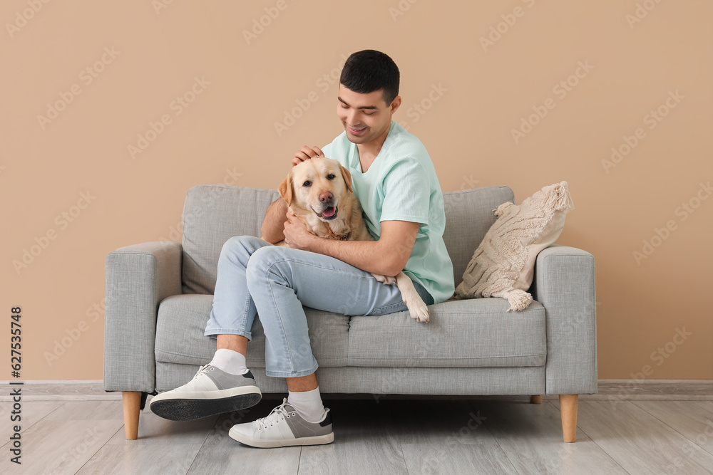 Young man with his Labrador dog sitting on sofa near beige wall