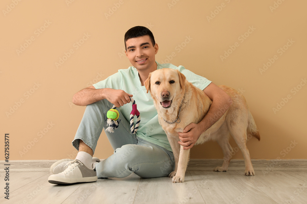 Young man with toy and his Labrador dog sitting near beige wall