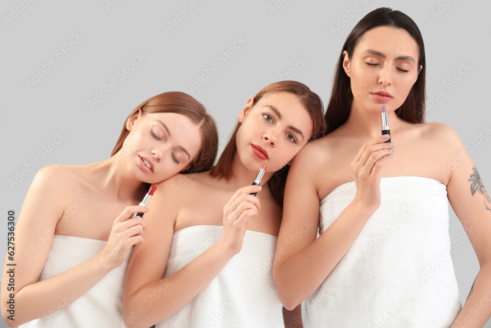 Young women with lipsticks on grey background