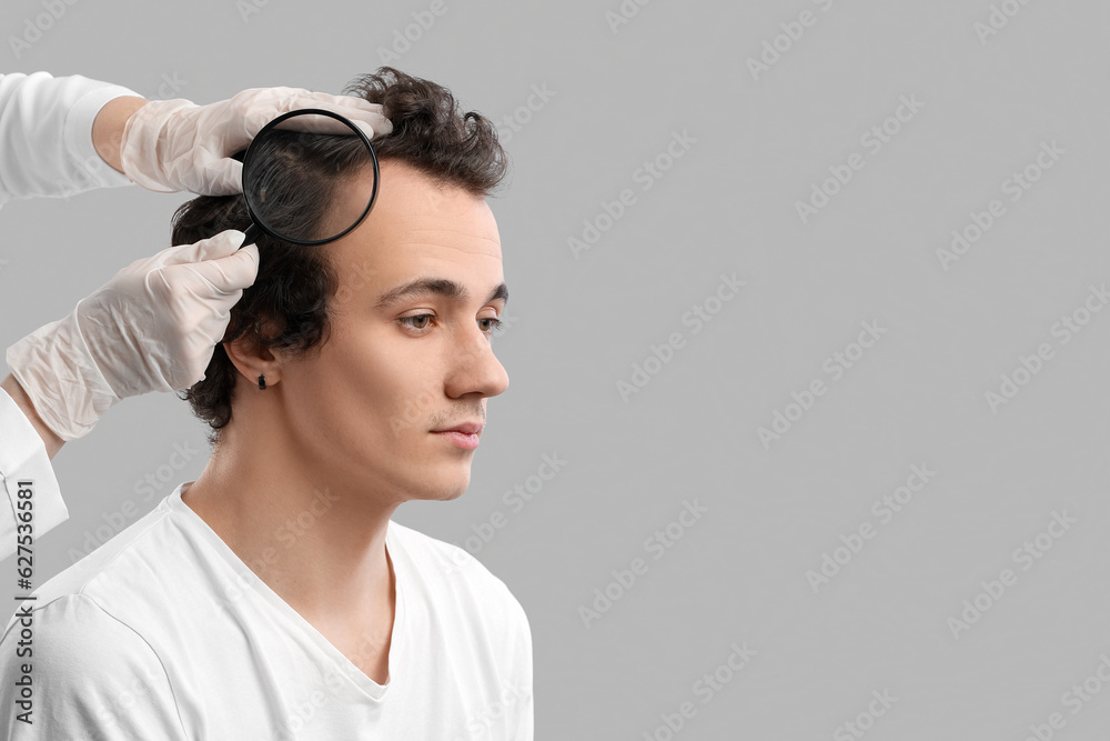 Doctor examining young man with hair loss problem on grey background