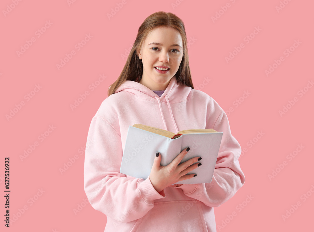 Teenage girl reading book on pink background