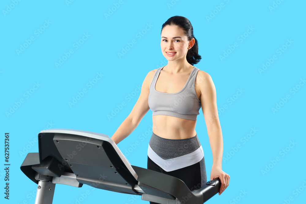 Beautiful woman training on treadmill against blue background