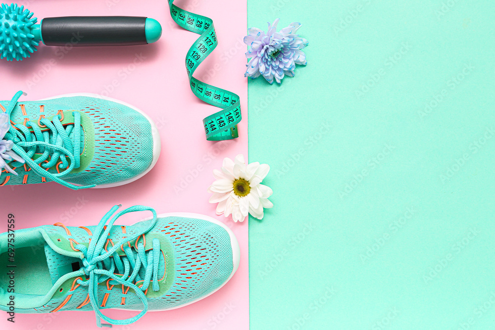 Sneakers with spring flowers, massage roller and tape measure on color background