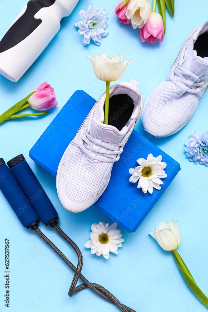 Sneakers with sports equipment and spring flowers on blue background