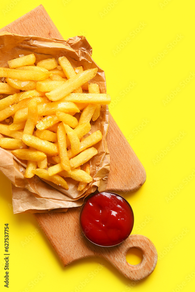 Wooden board with tasty french fries and ketchup on yellow background