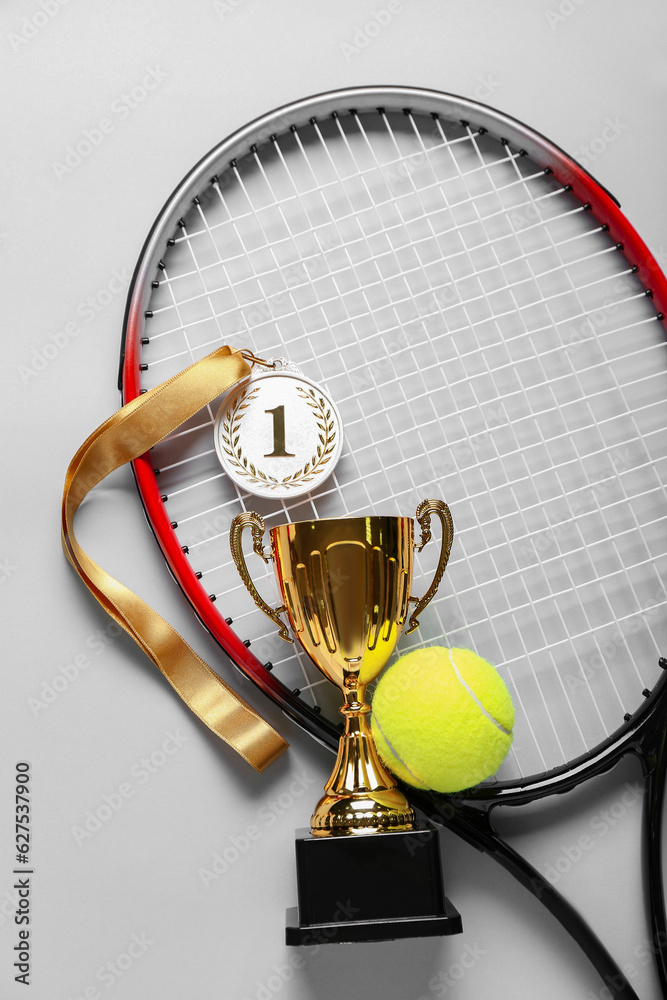 Gold cup with first place medal, tennis racket and ball on light background