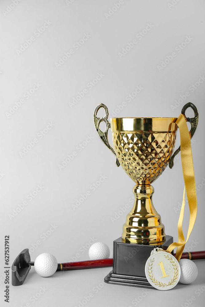 Gold cup with first place medal, golf club and balls on light background