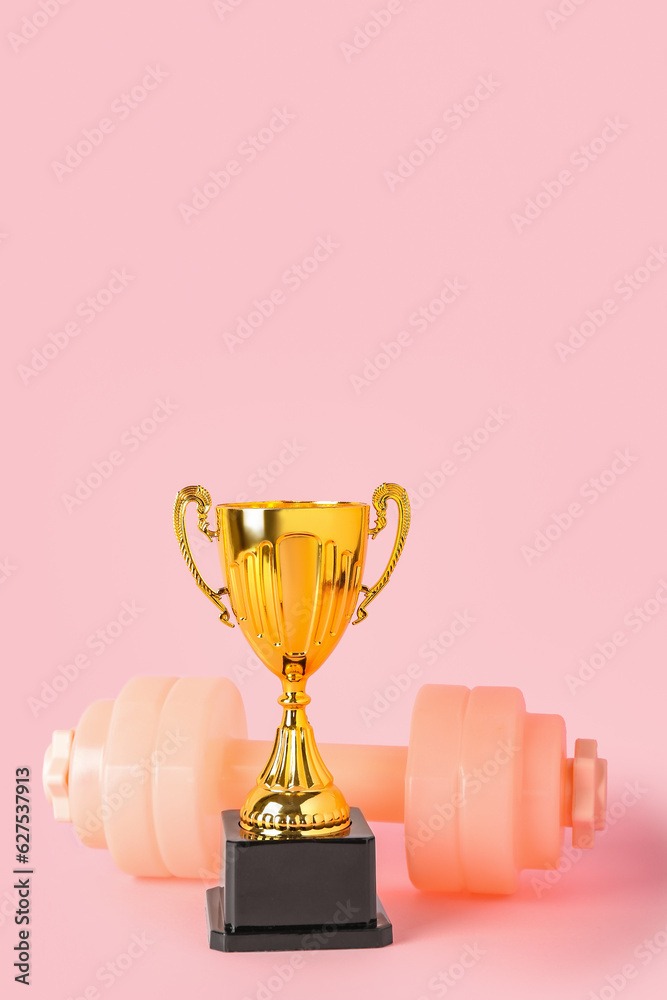 Gold cup with dumbbell on pink background